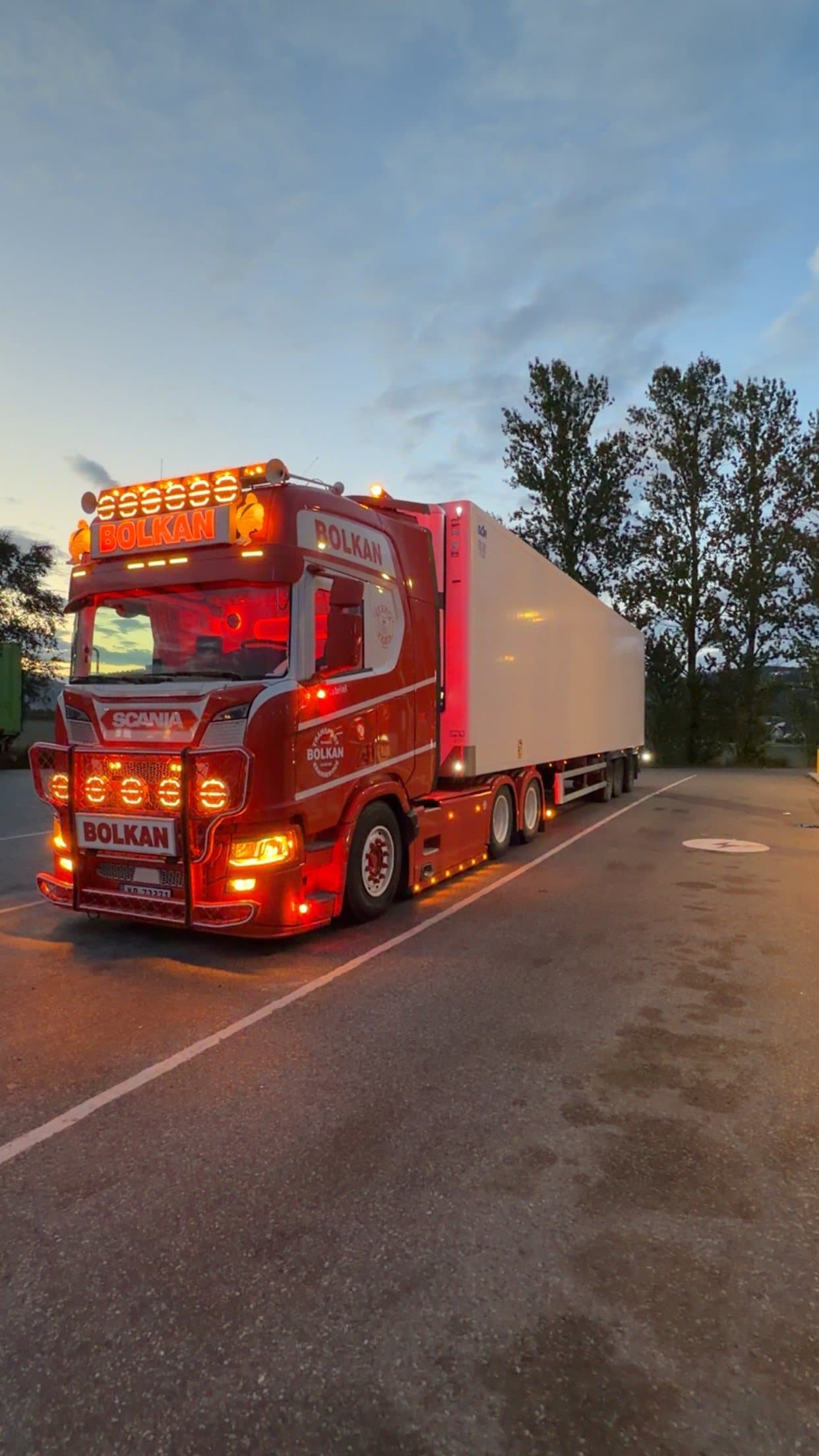 Bolkan Scania med lukket semitrailer og lysene på i skumringen