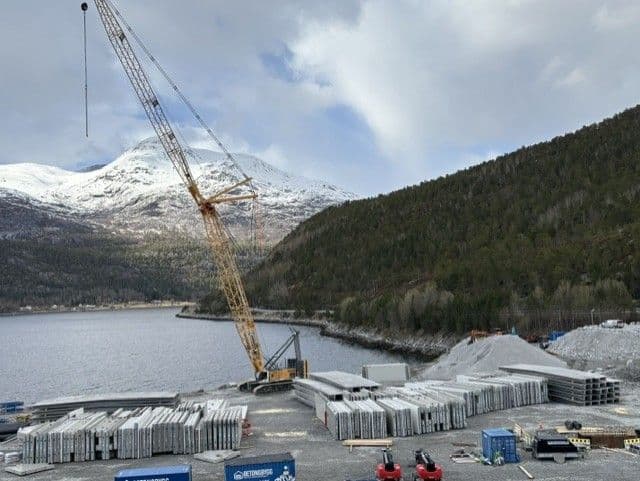 Beltekran og betongelementer på montasjeplassen ved fjorden i Nordland