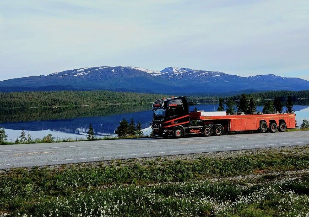 Svart Bolkan Scania med oransje henger ved et fjellvann
