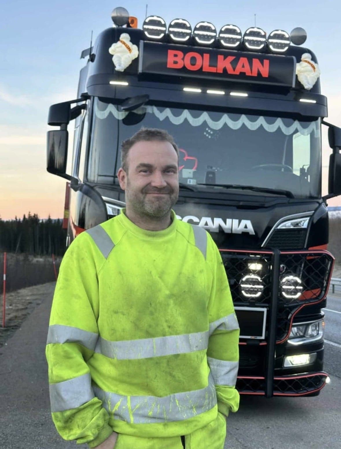 Sjåfør i gul arbeidsgenser foran en svart Bolkan Scania