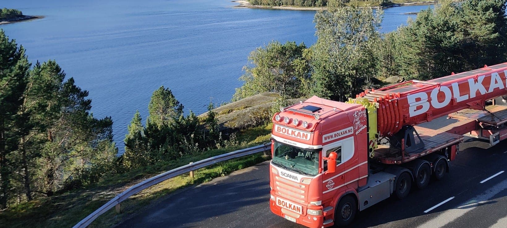 Bolkan Scania-vogntog med rød last merket Bolkan på en vei langs en fjord