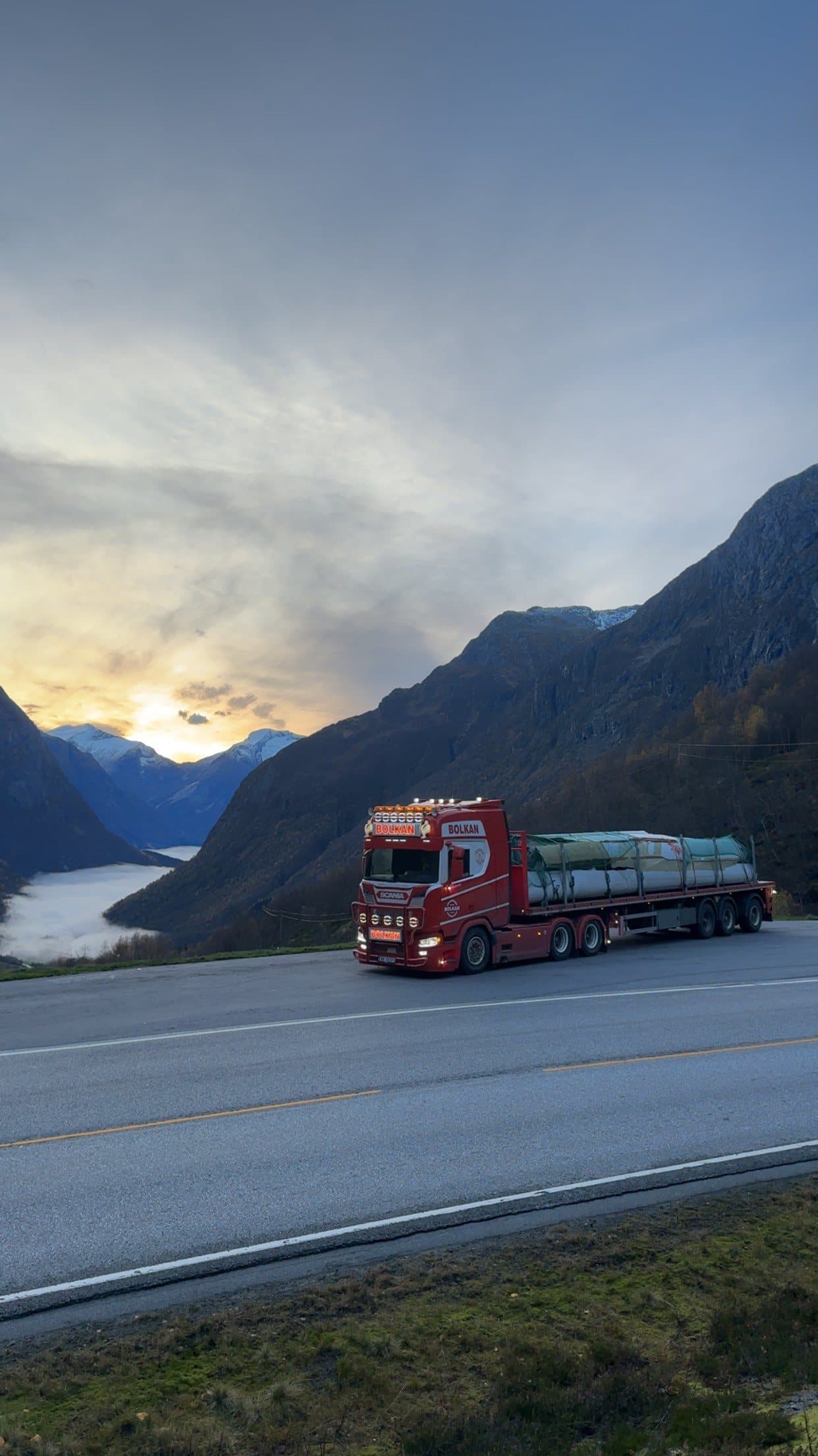 Bolkan Scania med presenningsdekket last på fjellvei over en fjord