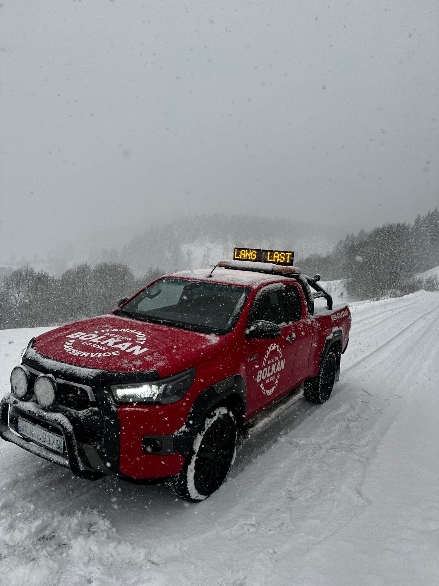 Bolkans varselbil med skiltet Lang last på taket på en snødekt vei