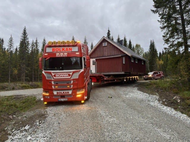 Bolkan Scania med ei rød hytte på hengeren på en grusvei i skogen i Lierne